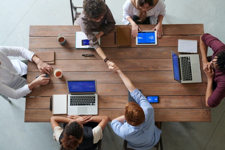 a group of people sitting around a table with laptops and papers on it